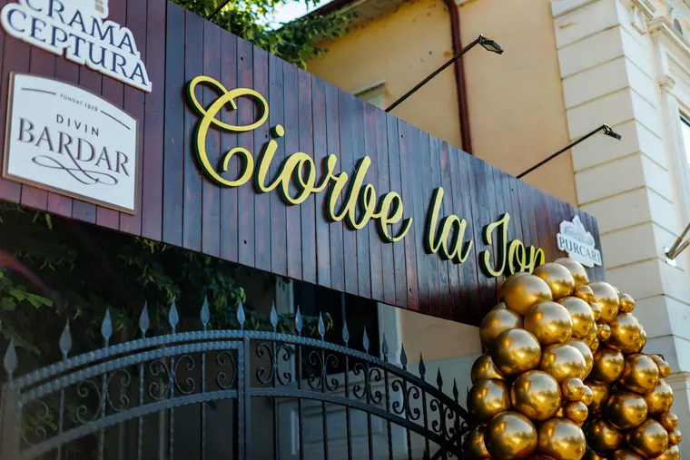 Firma de lemn cu numele Ciorbe La Ion, scris cu litere aurii, lângă un buchet de baloane aurii