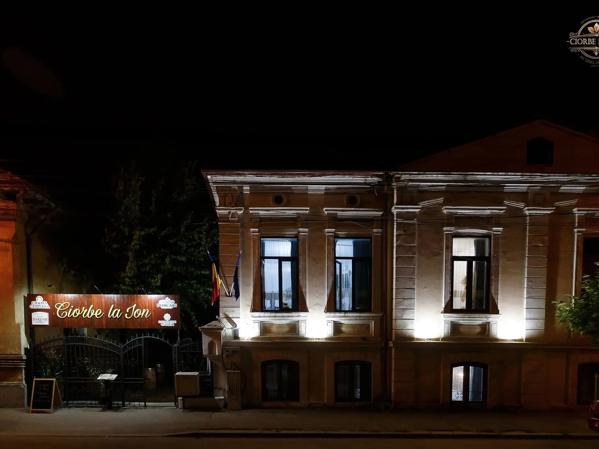 Fațada restaurantului luminată seara, cu firma aprinsă