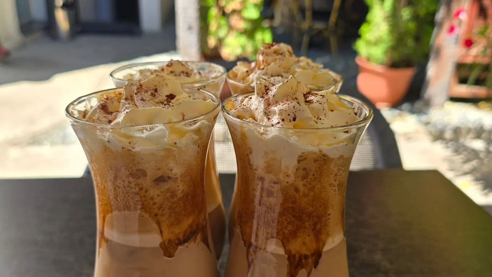 Trei pahare de cafea cu frișcă, pe o masă de pe terasă